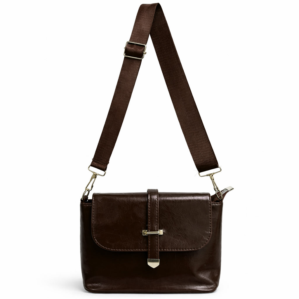 A classic women's crossbody bag in premium leather, featuring a stylish flap design, a distinctive silver metal clasp, and a wide, adjustable strap.